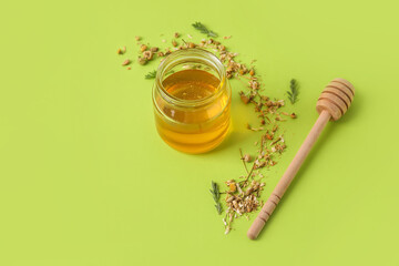 Jar of sweet honey and dried chamomile flowers on color background