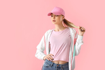Woman in baseball cap touching hair on pink background