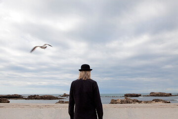 Morocco, Essaouira, rear view of man wearing a bowler hat standing at the sea