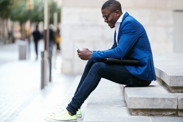 Young businessman wearing blue suit jacket, sitting on step and using smartphone