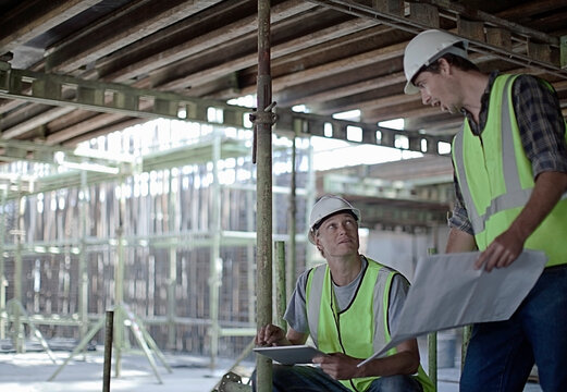 Male construction workers holding digital tablet while planning with coworker at construction site