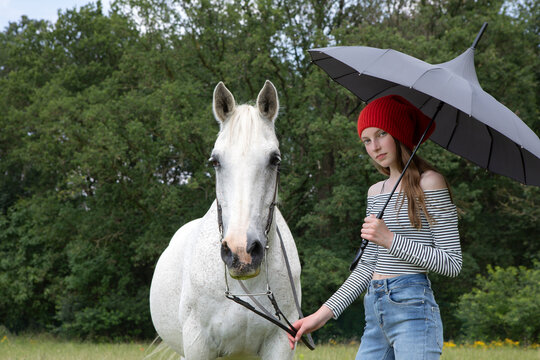 Portrait of teenage girl standing on a meadow with horse and umbrella