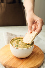 Man eating tasty baba ghanoush with cracker at table, closeup