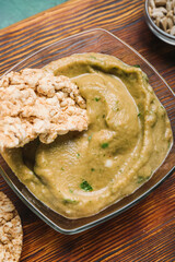 Bowl with tasty baba ghanoush and rice crackers on wooden board, closeup