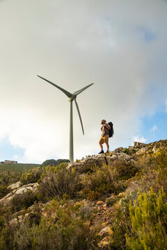 Spain, Andalusia, Tarifa, man on a hiking trip standing on rock with wind turbine in background