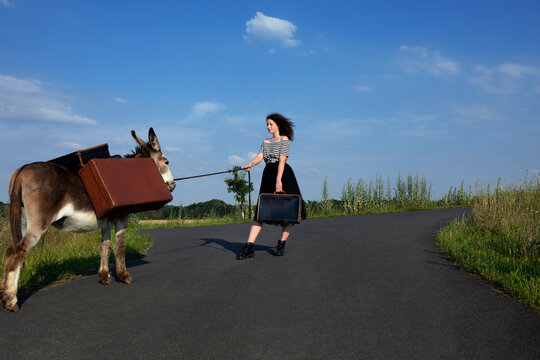 Young woman on country road with donkey carrying baggage