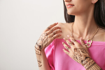 Beautiful Indian woman with henna tattoo on light background