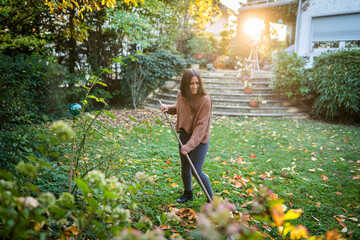 Happy woman sweeping garden with broom in back yard