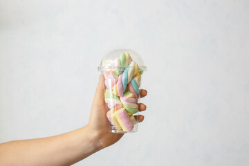Female hand holding plastic cup with tasty marshmallows on white background