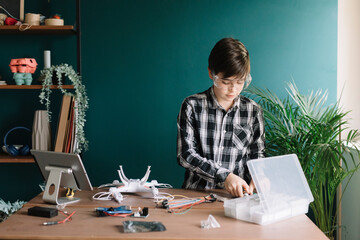 Boy making quadcopter on table while standing against wall at home