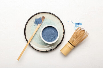 Bowl of powdered blue matcha tea, chashaku and chasen on light background