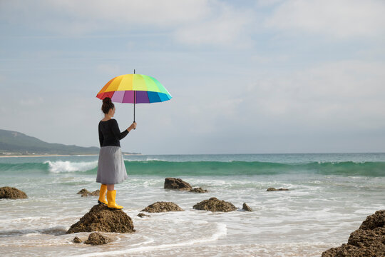 Woman with colorful umbrella standing on a stone at the beach