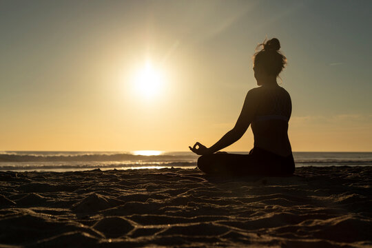 Woman meditating on the beach against evening sun
