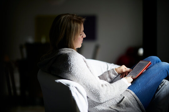 Woman sitting in armchair, reading e-book