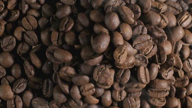Close up top down shot of brown coffee beans on a roasting pan, light smoke being released as the beans are slowly roasted to its familiar coffee characteristics