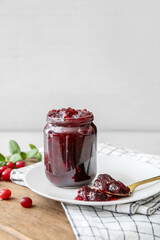 Jar of tasty cranberry jam on light background