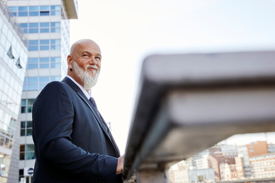 Elegant businessman leaning on railing  in the city, looking sceptical