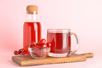 Cup and bottle of healthy dogwood berry drink on color background