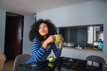 Portrait of young woman drinking coffee and eating an apple at home