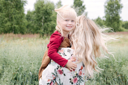 Young woman with blond hair carrying cute daughter while standing in oats field