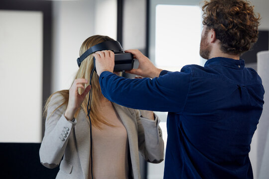 Businessman applying VR glasses on businesswoman in office