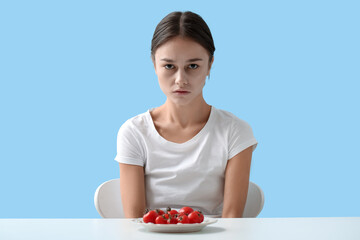Young woman at table against color background. Anorexia concept