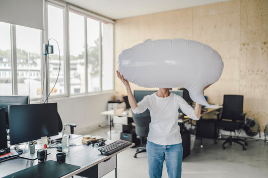 Woman standing in office, holding inflatable speech bubble in front of her face