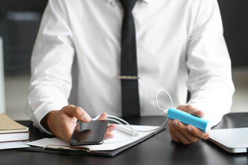 Young businessman with phone and power bank in office