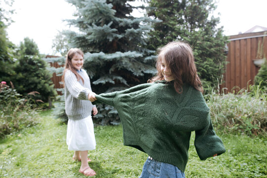 Playful girl pulling sister's sweater sleeve at back yard