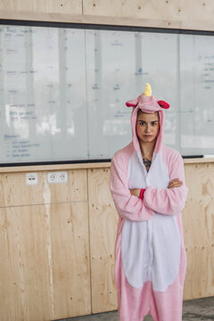 Woman wearing unicorn onesie, standing in front of whiteboard, looking stubborn