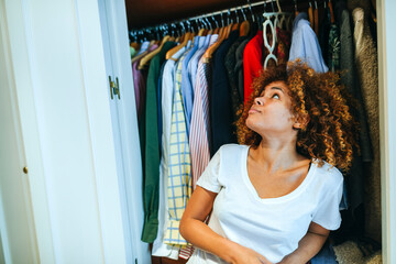 Young woman with curly hair at home looking at clothing in her wardrobe