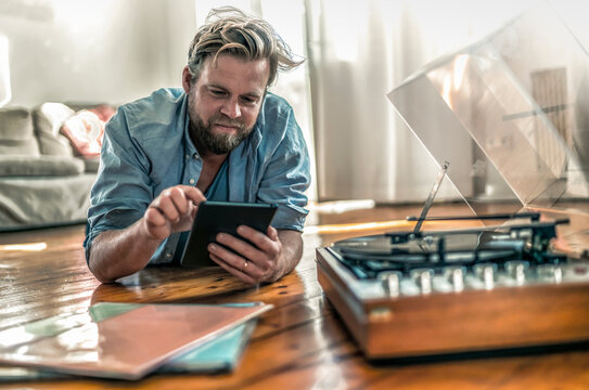 Man lying on the floor at home with tablet and record player