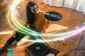 Young woman sitting on the floor at home with record and record player surrounded by a light trail