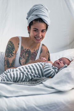 Portrait of smiling tattooed young woman with her baby in canopy bed
