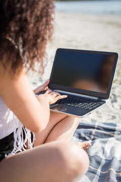 Crop view of young woman sitting on blanket on the beach using laptop
