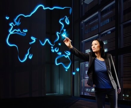 Businesswoman painting a worldmap with light, pointing on Japan