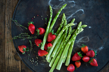 Thyme, peppercorn, asparagus stalks and fresh strawberries on rustic baking sheet