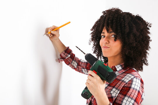 Woman using portable drill, marking with pencil on a wall