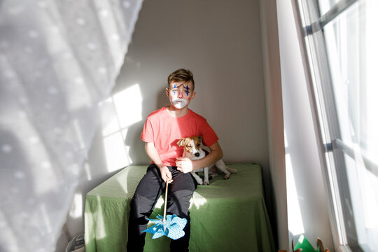 Portrait of boy made up as a clown with dog and pin wheel at home