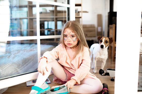 Blond girl made up as butterfly sitting on the ground, jack russel terrier in the background