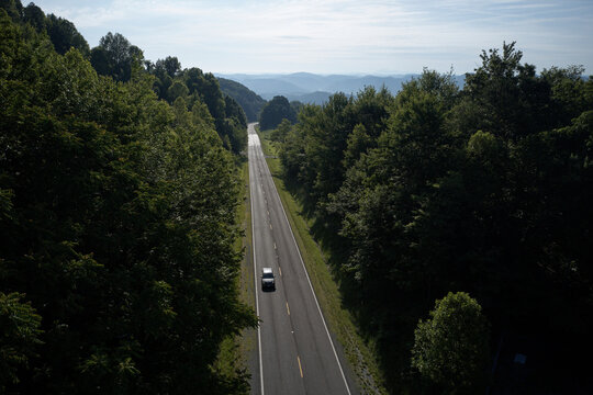 Aerial view of lone car driving along U.S. Route 58 stretching across green alpine forest