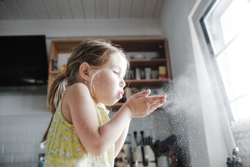 Little girl blowing flour in the air in the kitchen