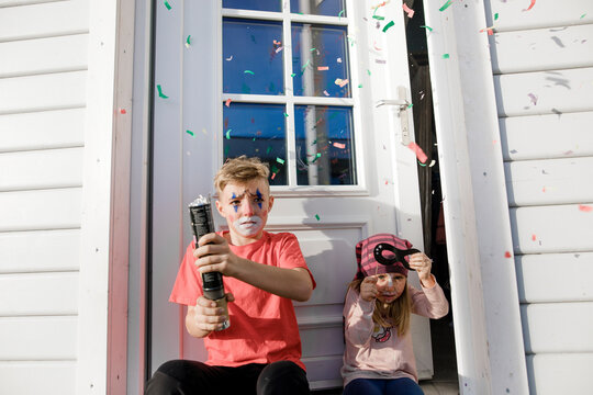 Brother and little sister made up for carnival sitting in front of entry door