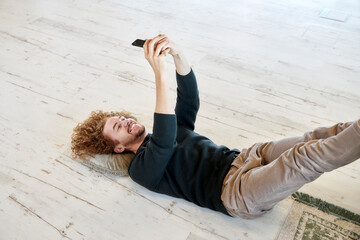 Smiling man taking selfie through smart phone lying down on floor at home