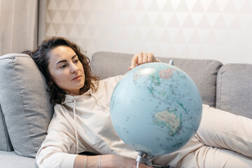 Portrait of woman lying on the couch at home looking at globe