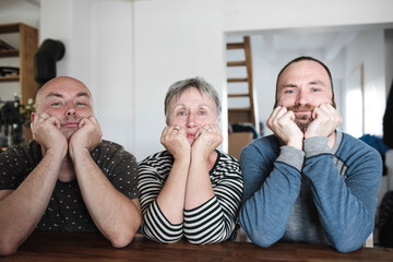 Portrait of adult sons with senior mother sitting at table at home with head in hands