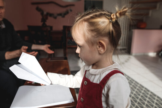 Girl holding paper plane in living room with grandfather in background