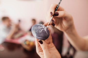Woman painting Easter egg at home with children in background