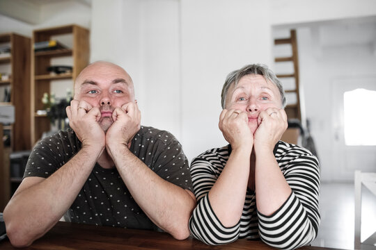 Portrait of adult son with senior mother sitting at table at home with head in hands