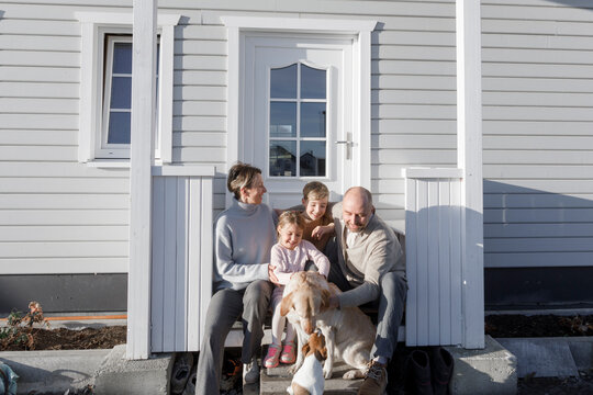Happy family with two children and two dogs sitting in front of their house